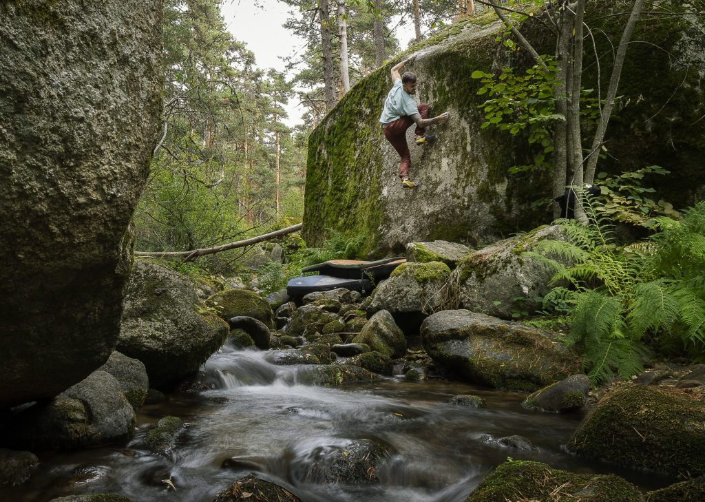 Escalador practicando boulder en La Pedriza, rodeado de vegetación y un arroyo, durante el Festival La Pedriza 2025 impulsado por el Ayuntamiento de El Boalo, Cerceda y Mataelpino.