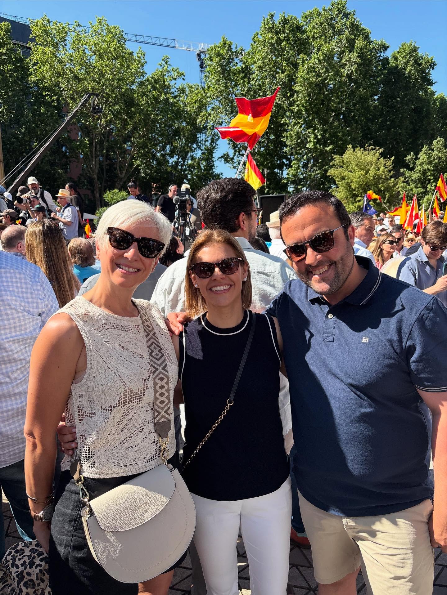 Tres sonrientes ciudadanos, dos mujeres y un hombre, posando en medio de una multitudinaria manifestación con banderas de España, en el contexto de "La España que dice basta ya".