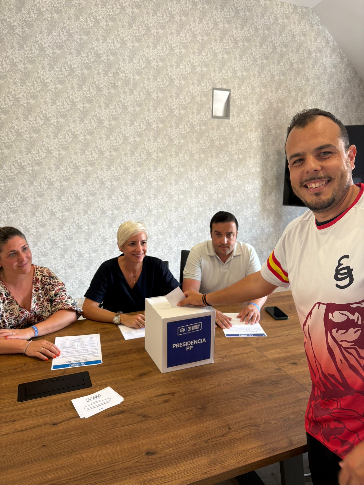 Un afiliado del Partido Popular, con una camiseta de España, depositando su voto en la urna de "PRESIDENCIA PP" durante la jornada electoral en El Boalo, Cerceda y Mataelpino.