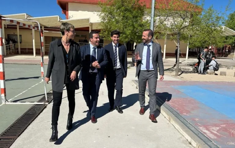 El Alcalde Sergio Yunquera y otros representantes caminan al aire libre, posiblemente en el exterior de un colegio, con el sol iluminando la escena.