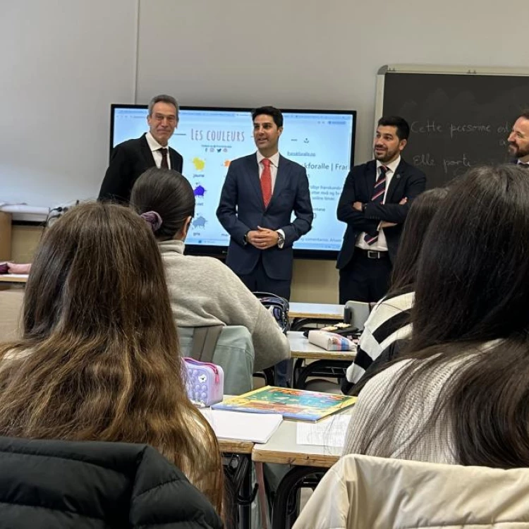 Cuatro hombres, incluido el alcalde Sergio Yunquera, de pie frente a una pizarra interactiva en un aula, con estudiantes sentados de espaldas.