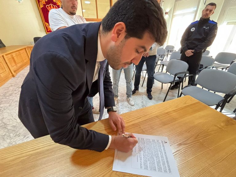 El alcalde de El Boalo, Cerceda y Mataelpino, Sergio Yunquera, vestido de traje, firmando un documento importante sobre una mesa de madera en una sala.
